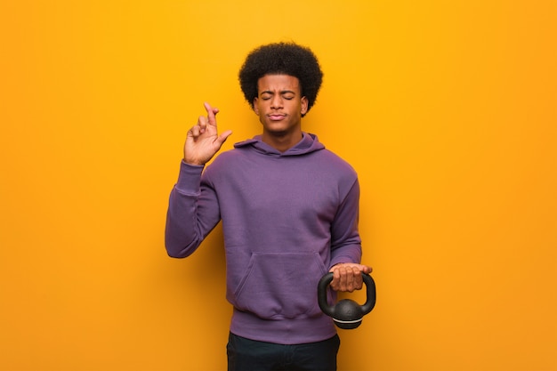 Jeune homme de remise en forme afro-américain tenant un haltère traversant les doigts pour avoir de la chance