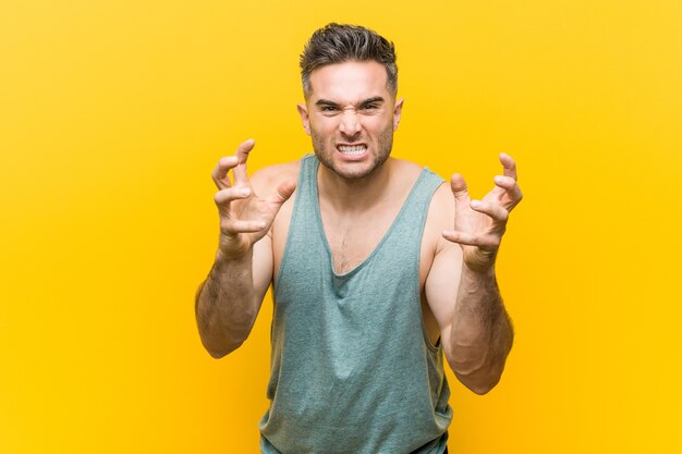 Jeune homme de remise en forme contre un espace jaune bouleversé en criant avec des mains tendues.