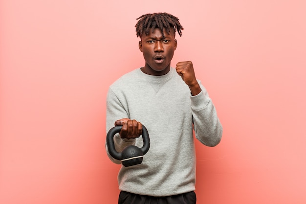 Jeune homme de remise en forme tenant un haltère montrant le poing à la caméra, une expression faciale agressive.