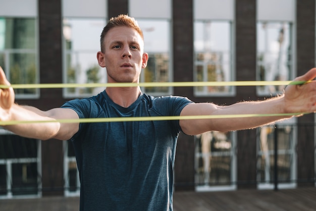 Jeune homme de remise en forme en vêtements de sport faisant des exercices avec une bande élastique de résistance à la main