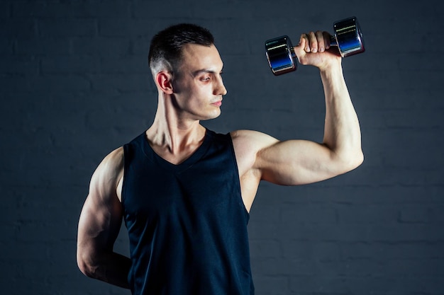 Le jeune homme renforce les muscles des mains des haltères dans le gymnase sur un fond noir