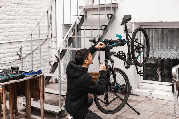 Un jeune homme répare un vélo dans le jardin de la maison