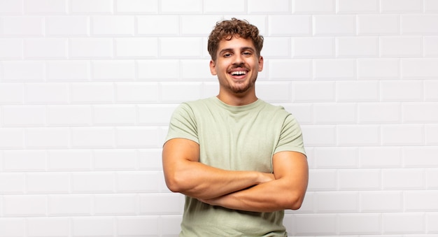 Jeune homme ressemblant à un réalisateur heureux, fier et satisfait souriant, les bras croisés