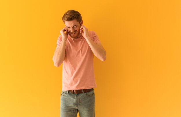 Jeune homme rousse couvrant les oreilles avec les mains