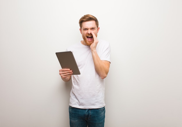 Jeune homme rousse criant quelque chose de joyeux à l'avant. Tenant une tablette.