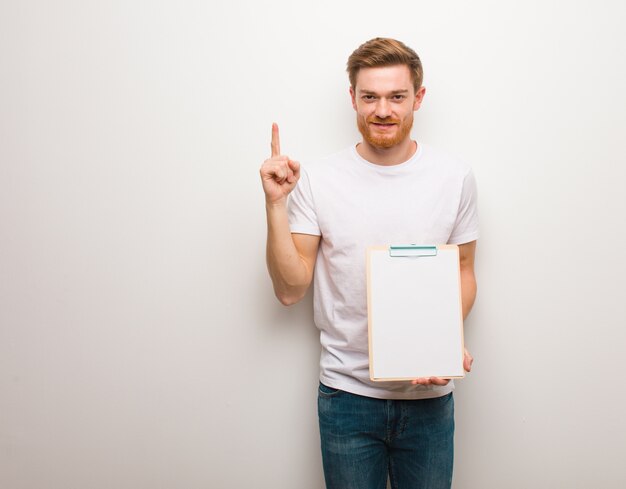 Jeune homme rousse montrant le numéro un. Il tient un presse-papiers.