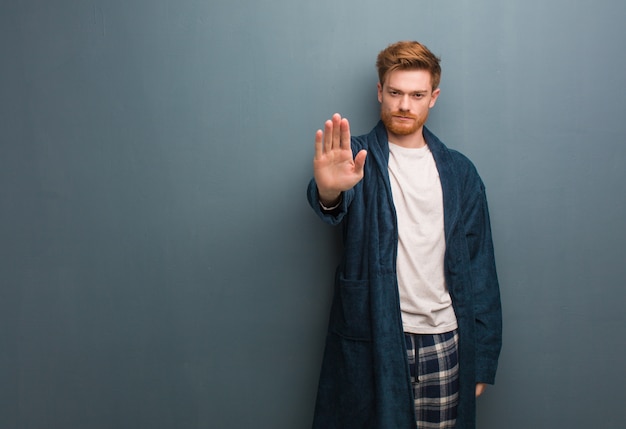 Jeune homme rousse en pyjama mettant la main devant