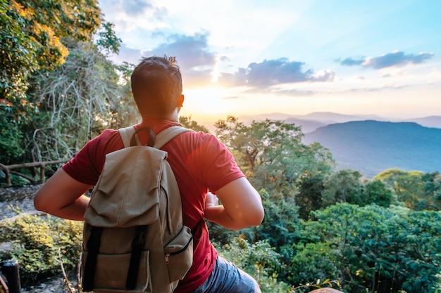 Jeune homme routard assis et regardant autour des falaises rocheuses dans la forêt avec le coucher du soleil après avoir atteint l'espace de copie de destination