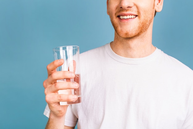 un jeune homme roux dans un t-shirt blanc buvant de l'eau dans un verre.