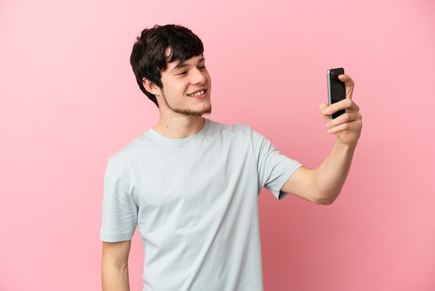 Jeune homme russe isolé sur fond rose faisant un selfie