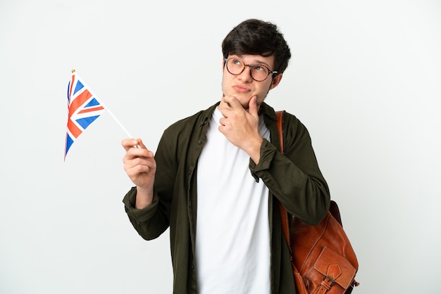 Jeune homme russe tenant un drapeau du Royaume-Uni isolé sur fond blanc ayant des doutes