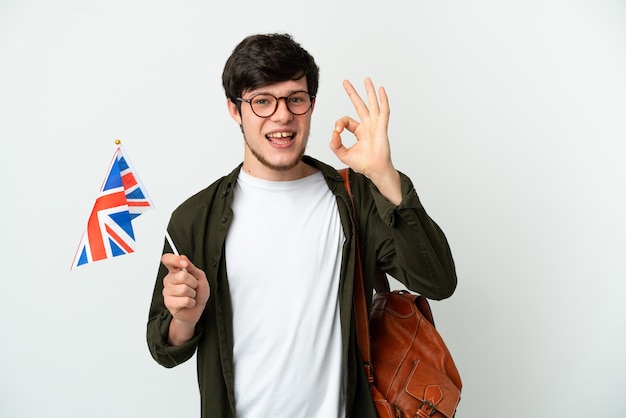 Jeune homme russe tenant un drapeau du Royaume-Uni isolé sur fond blanc montrant un signe ok avec les doigts