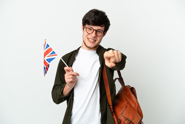 Jeune homme russe tenant un drapeau du Royaume-Uni isolé sur fond blanc pointant vers l'avant avec une expression heureuse