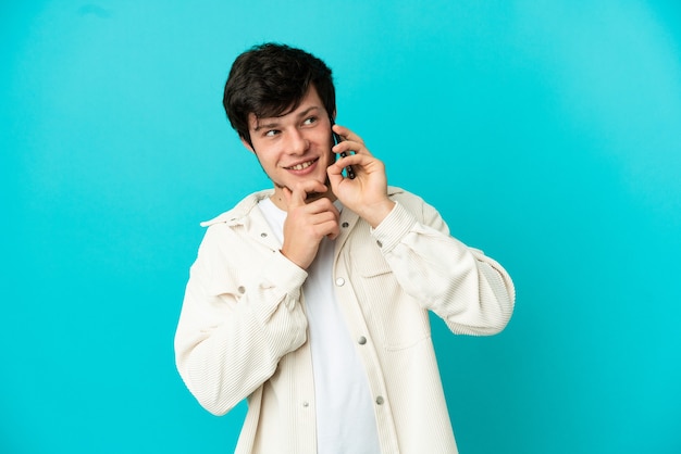 Jeune homme russe utilisant un téléphone portable isolé sur fond bleu et levant