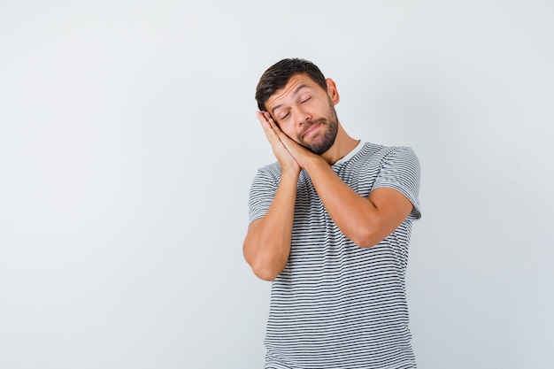 Jeune homme s'appuyant sur les paumes comme oreiller en t-shirt et ayant l'air endormi. vue de face.