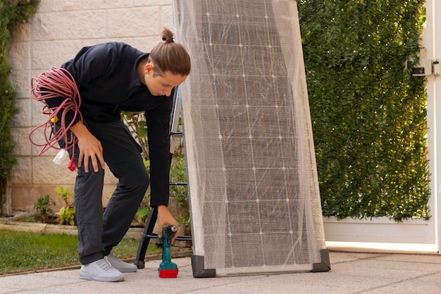 Un jeune homme s'est accroupi pour ramasser un tournevis électrique pour installer le nouveau panneau solaire