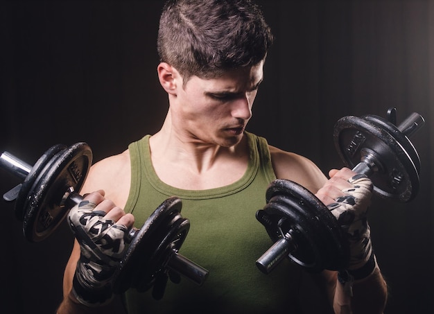 Un jeune homme s'exerce avec des haltères alors qu'il se tient contre un fond noir