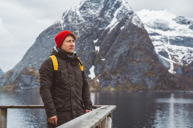 Jeune homme avec un sac à dos debout sur une jetée en bois le fond des montagnes enneigées et du lac