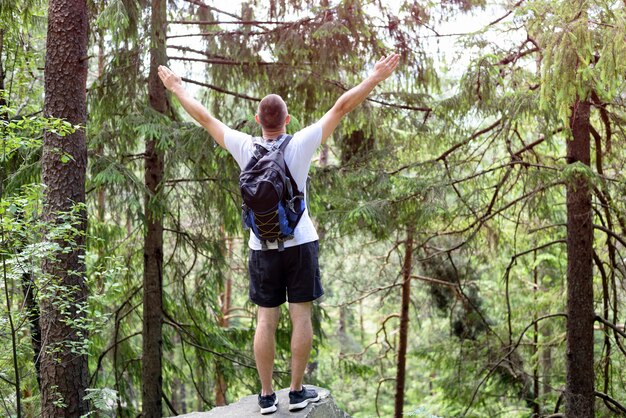 Jeune homme avec un sac à dos, debout les mains sur un rocher dans la forêt de conifères