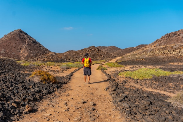 Un jeune homme avec un sac à dos jaune sur le sentier en direction nord vers Isla de Lobos, le long de la côte nord de l'île de Fuerteventura, îles Canaries. Espagne