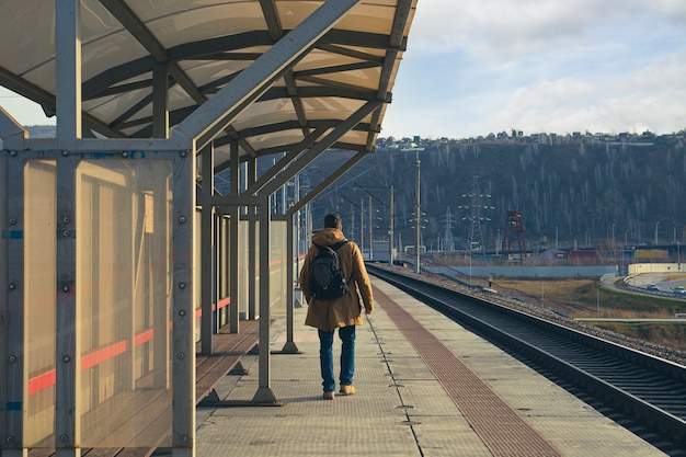 Un jeune homme avec un sac à dos marche le long du quai de la gare. Transports ferroviaires, voyages, communications.