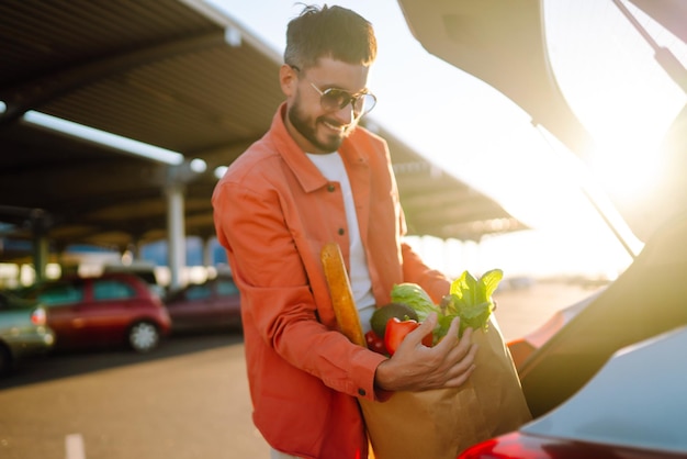 Jeune homme avec sac plein de légumes près de la voiture Bel homme après le shopping