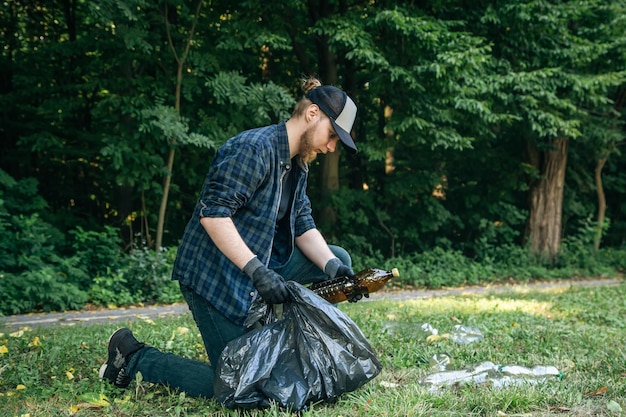 Un jeune homme avec un sac poubelle dans la forêt nettoie les bouteilles en plastique