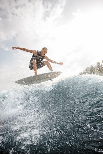 Jeune homme sautant sur le wakeboard blanc dans l'eau bleue contre le ciel gris