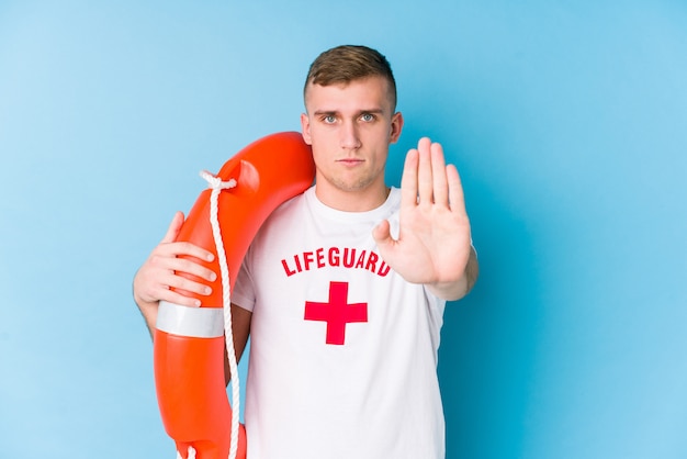 Jeune homme sauveteur tenant un flotteur de sauvetage debout avec la main tendue montrant le panneau d'arrêt, vous empêchant.