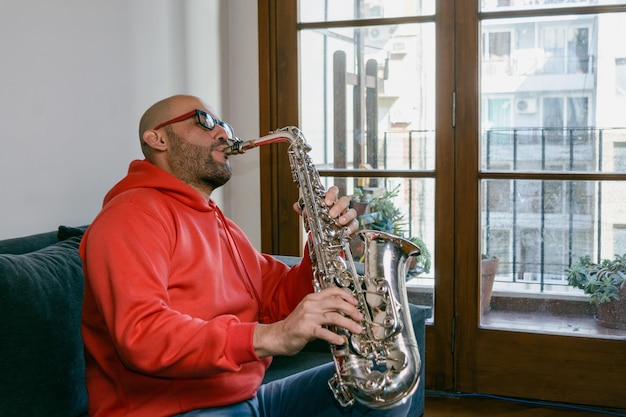 jeune homme saxophoniste latin à la maison assis inspiré en jouant de la musique