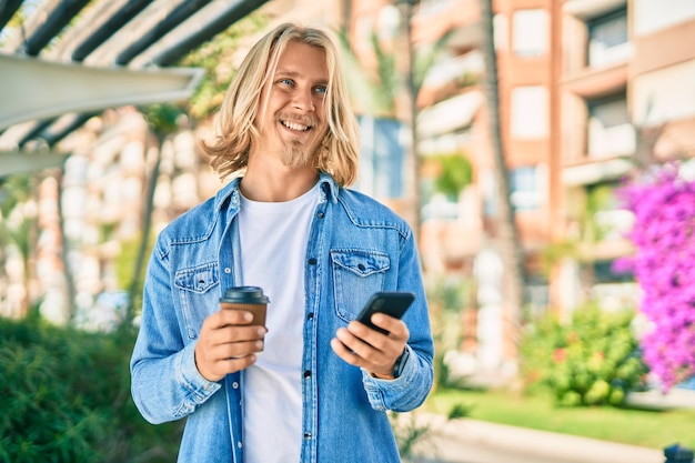 Jeune homme scandinave blond utilisant un smartphone buvant du café à la ville.