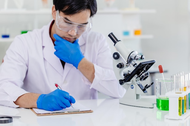 Jeune homme scientifique asiatique portant un uniforme de laboratoire blanc testant la formule médicale de recherche au laboratoire