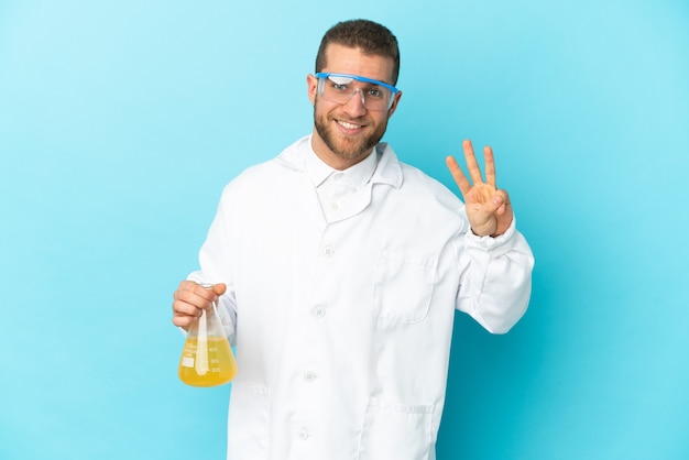 Jeune homme scientifique caucasien isolé sur bleu heureux et comptant trois avec les doigts