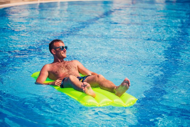 Un jeune homme se baigne dans la piscine sur un matelas gonflable jaune Détendez-vous au soleil en vacances