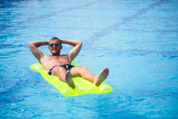 Un jeune homme se baigne dans la piscine sur un matelas gonflable jaune