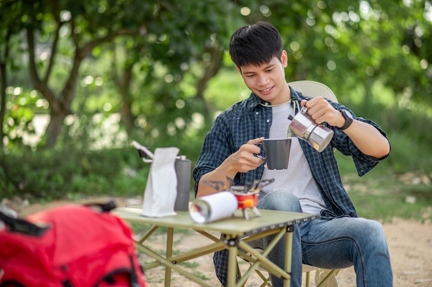 Jeune homme se détendre avec un café au parc naturel pendant le camping