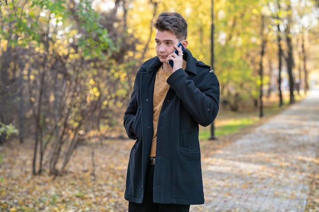 un jeune homme se promène dans un parc en automne et parle au téléphone