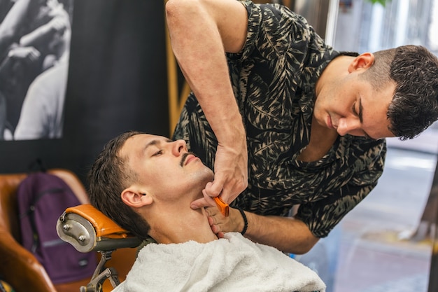 Jeune homme se raser à l'ancienne au salon de coiffure