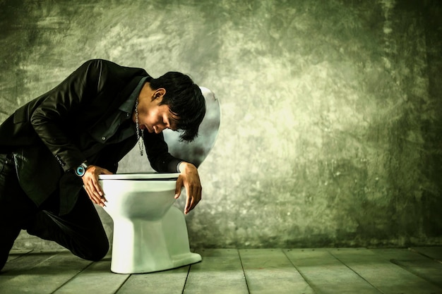Un jeune homme se sent malade sur les toilettes contre le mur.