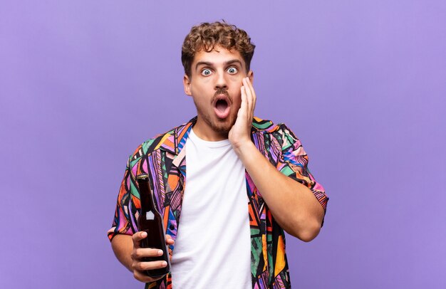 Jeune homme se sentant choqué et effrayé, l'air terrifié avec la bouche ouverte et les mains sur les joues. concept de vacances