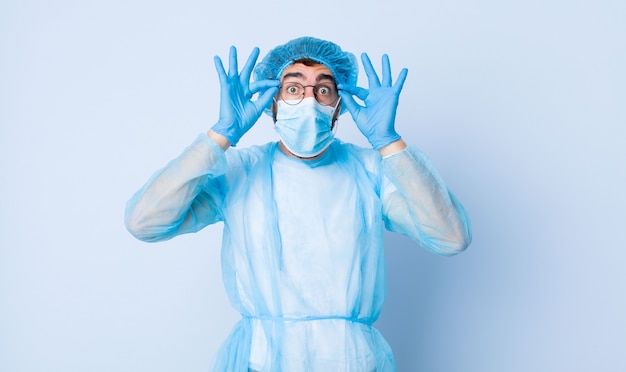 Jeune homme se sentant choqué, étonné et surpris, tenant des lunettes avec un regard étonné et incrédule. concept de coronavirus