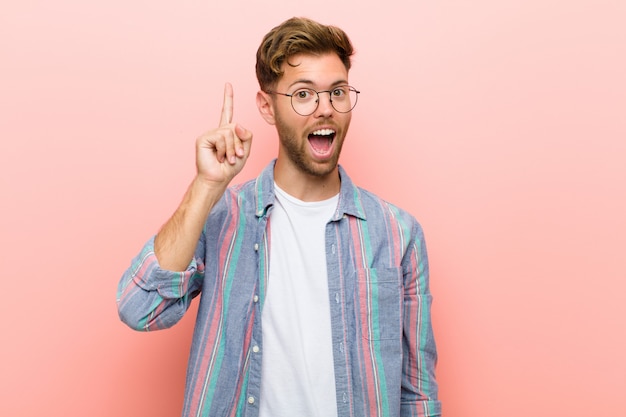 Jeune homme se sentant comme un génie heureux et excité après avoir réalisé une idée, levant joyeusement le doigt, eureka! sur fond rose