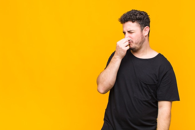 Jeune homme se sentant dégoûté, tenant le nez pour éviter de sentir une odeur nauséabonde et désagréable