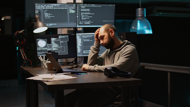Jeune homme se sentant fatigué et travaillant sur le code de programmation, tapant les informations de la base de données et le script html sur un ordinateur portable. Adulte s'endormant au bureau, épuisé à l'aide de la fenêtre du terminal. Prise de vue à main levée.