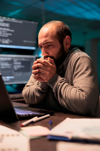 Jeune homme se sentant froid et buvant une tasse de café, utilisant une boisson chaude pour se réchauffer au bureau tard dans la nuit. Codeur masculin servant un rafraîchissement à la caféine et programmant une nouvelle interface utilisateur.