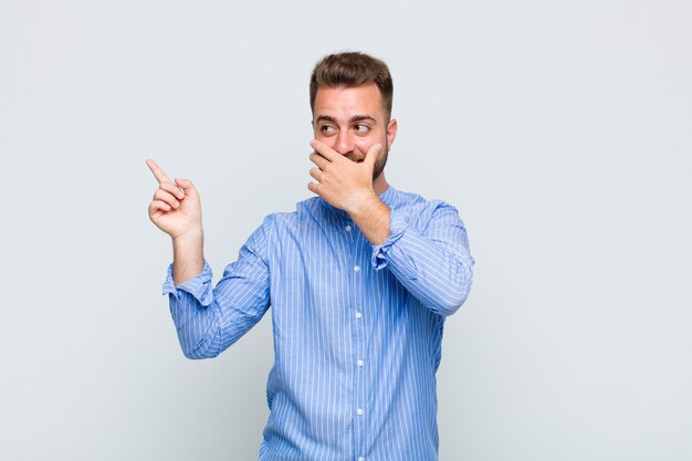 Jeune homme se sentant heureux, choqué et surpris, couvrant la bouche avec la main et pointant vers l'espace de copie latérale