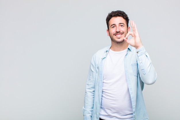 Jeune homme se sentant heureux, détendu et satisfait, montrant son approbation avec un geste correct, souriant