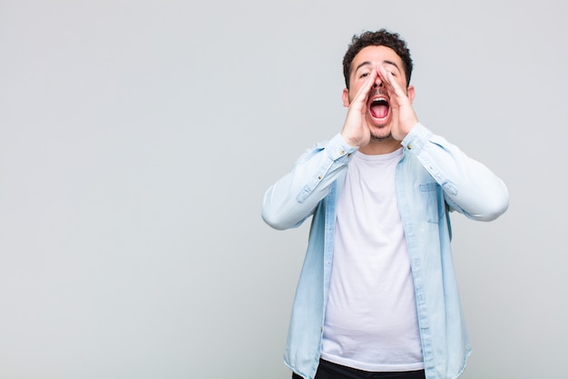 Jeune homme se sentant heureux, excité et positif, donnant un grand cri avec les mains à côté de la bouche, appelant