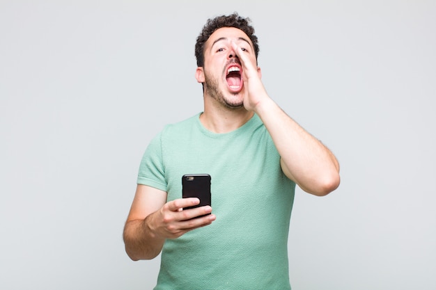 Jeune homme se sentant heureux, excité et positif, donnant un grand cri avec les mains à côté de la bouche, appelant