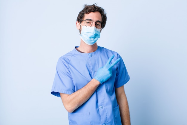 Jeune homme se sentant heureux, positif et réussi, avec la main en forme de v sur la poitrine, montrant la victoire ou la paix. concept de coronavirus